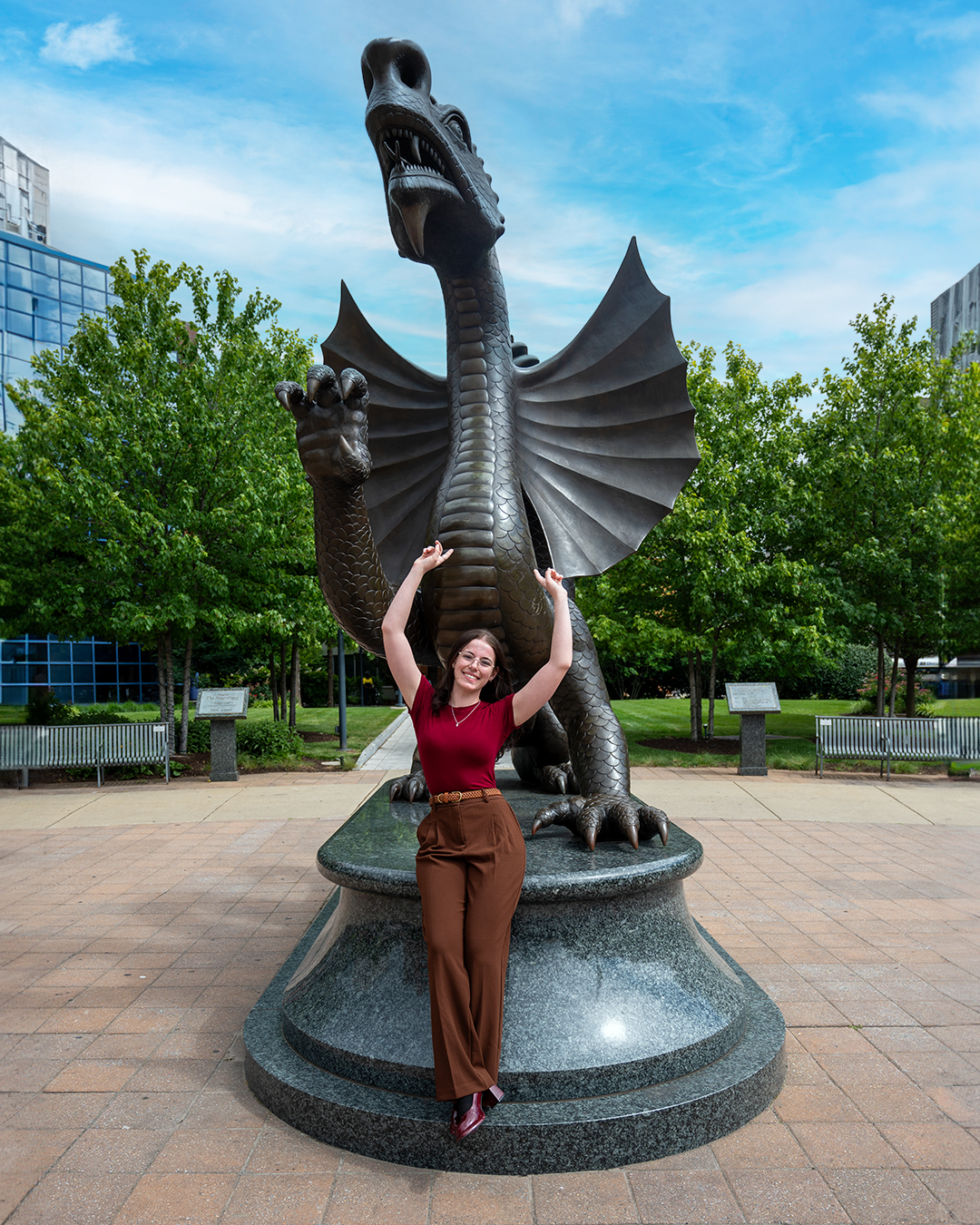Stephanie Bieder wearing red shirt and brown pants pointing up standing in front of Mario statue